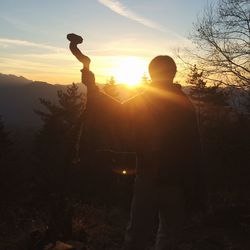 Silhouette man with arms raised against sky during sunset