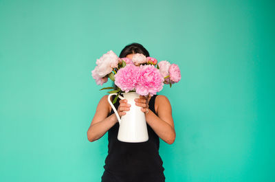 Woman holding flower vase while standing against green background