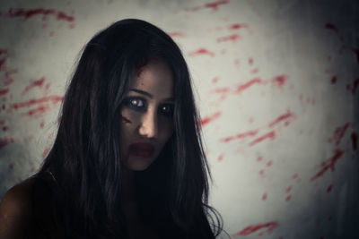 Portrait of young woman with spooky eyes standing against wall