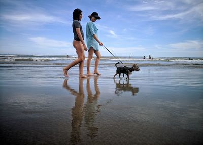 Mother and daughter with dog at beach against sky