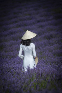 Rear view of woman wearing asian style conical hat while standing amidst flowering plants on field