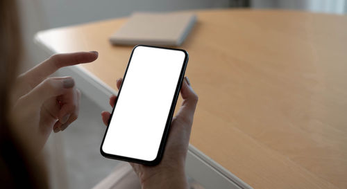 Close-up of hand holding smart phone on table