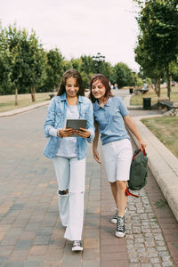 Two schoolgirls are holding a tablet in their hands and watching a video, laughing on the way 