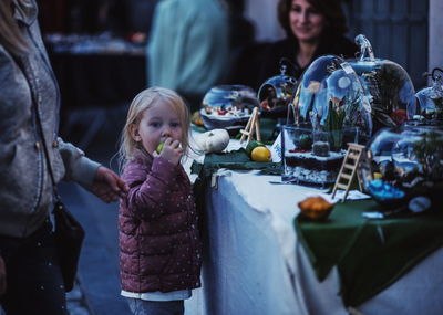 Side view of cute girl eating fruit while standing by table