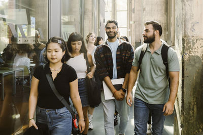 Smiling university student walking with male and female friends at college corridor