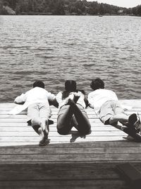 Rear view of people sitting on pier over lake