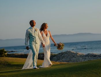 Side  view of bride and groom standing by sea against sky
