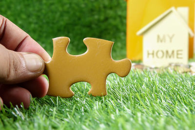 Cropped hand holding jigsaw piece against model house on field