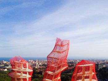 Artwork covered with red net by city against sky