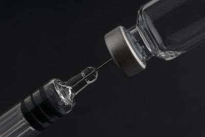 Close-up of syringe and vial against black background