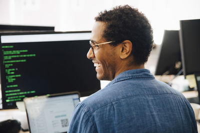 Rear view of cheerful male it professional looking away while sitting in creative office