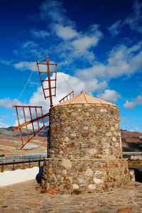 Traditional windmill at by mountains against cloudy sky