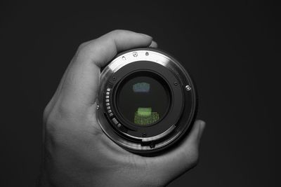 Cropped image of person holding lens against black background