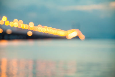 Close-up of hand against illuminated sea against sky