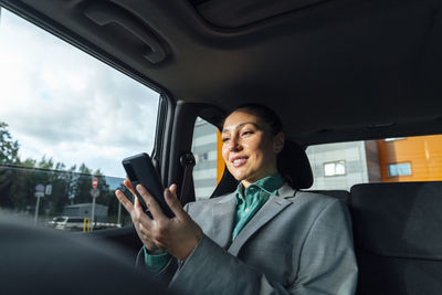 Happy businesswoman using smart phone sitting in car