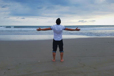 Rear view of man standing on sand at beach against sky