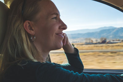 Smiling woman driving on road trip in desert with view out of drivers window.