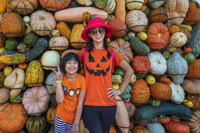 Portrait of smiling woman with daughter standing against pumpkins