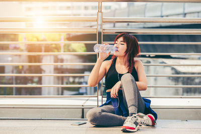 Full length of young woman drinking water on elevated walkway