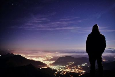 Rear view of silhouette man standing on mountain against sky at night