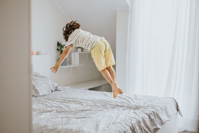 A little boy joyfully jumps on the bed in the bedroom. fun games at home. children's activity 