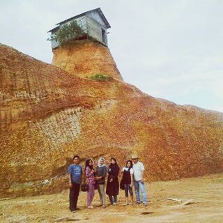 TOURISTS ON CLIFF BY MOUNTAINS AGAINST SKY