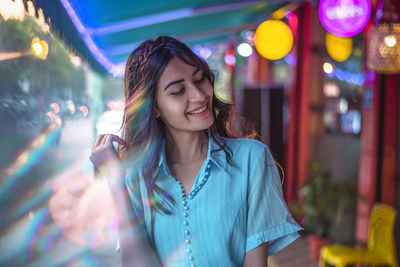 Beautiful young woman standing against illuminated lights