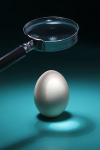 Magnifying glass over egg on blue table