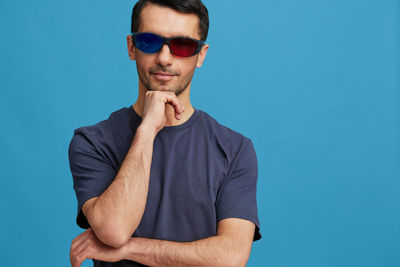 Portrait of young man wearing sunglasses against blue background