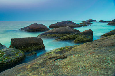 Scenic view of rocks in sea against blue sky