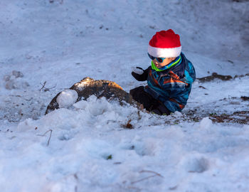 Boy sitting on snow outdoors during winter