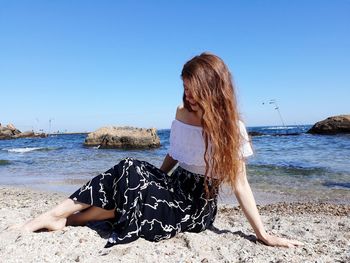 Young woman at beach against clear sky