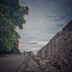 People walking on footpath by road against sky