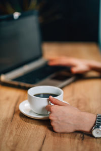 Cropped hands of businesswoman having coffee while using laptop in office