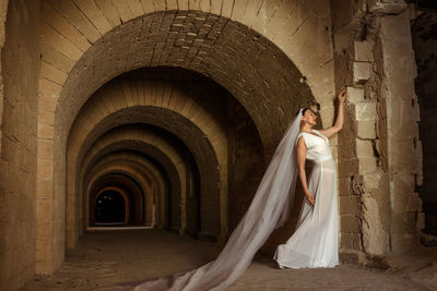 A sad elegant lady in white bride dress with a train languishes in the gloomy old castle