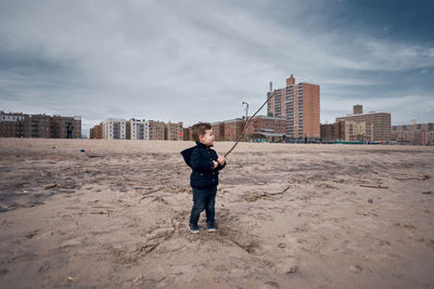 Happy young toddler running around the beach with a big branch