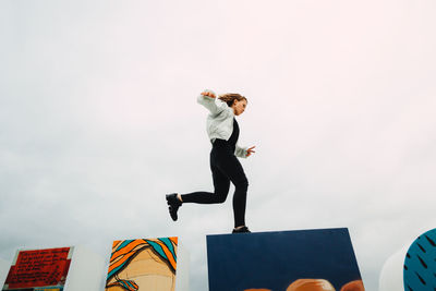 Low angle view of woman jumping over wall against sky