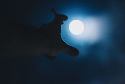 Silhouette hand against moon in sky