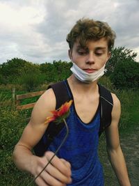 Portrait of a young man giving a flower standing on the nature against the background of the sky.