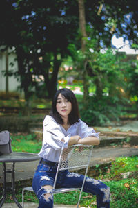 Portrait of young woman sitting on bench in park