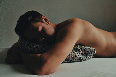 Side view of shirtless young man lying on bed at home