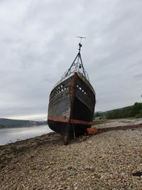 Abandoned boat on beach against sky