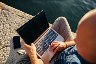 High angle view of man using laptop while sitting on retaining wall