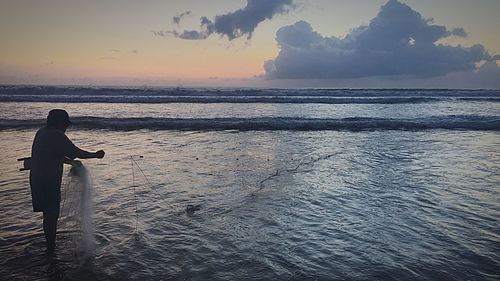 Silhouette man standing on beach against sky during sunset