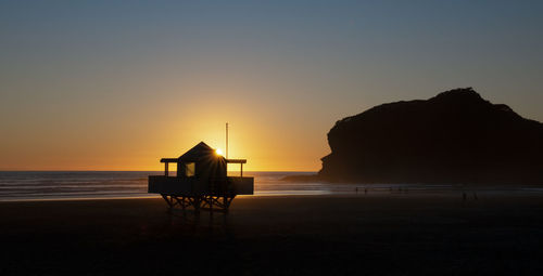 Silhouette lifeguard hut on beach against sky during sunset