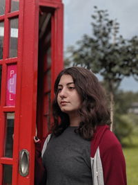 Young woman looking away while standing by telephone booth