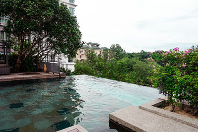 Swimming pool by trees and house against sky