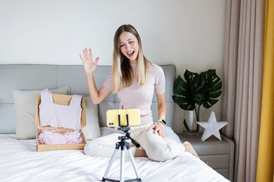 Young woman using digital tablet while sitting on bed at home