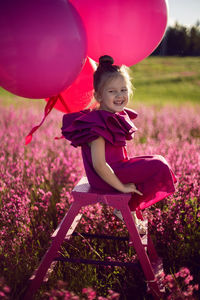  girl child of 5 years old is sitting on a pink stepladder,  dress in a field with pink flowers