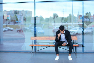 Full length of young man sitting on glass window